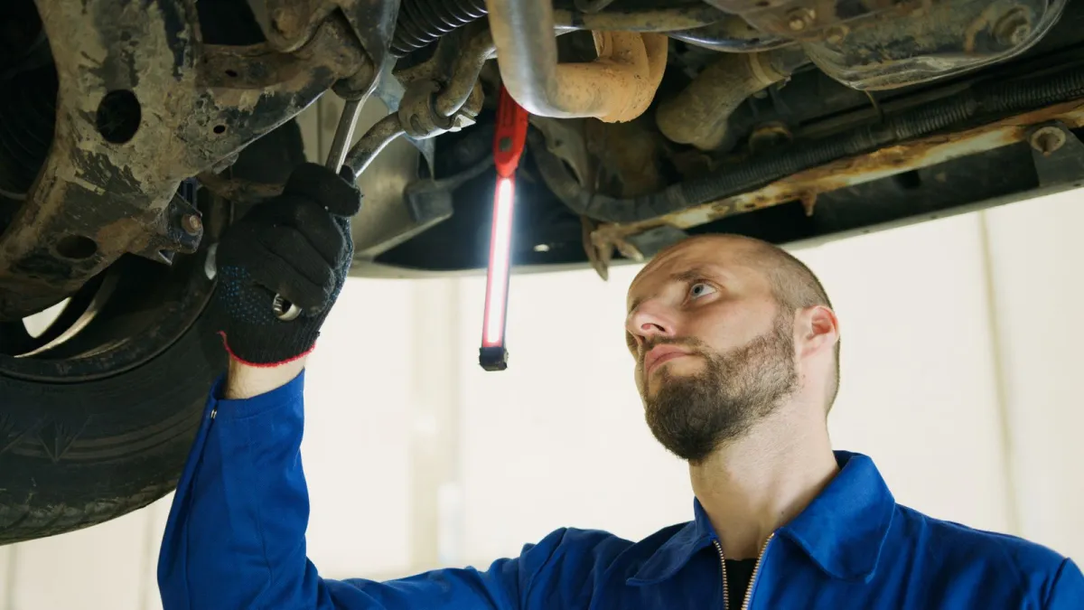 Mechanic inspecting the underside of a car with a hand lamp