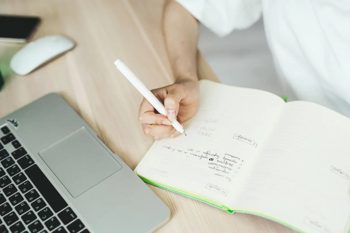 Laptop and notebook on a desk while a writer jots down blog headline ideas