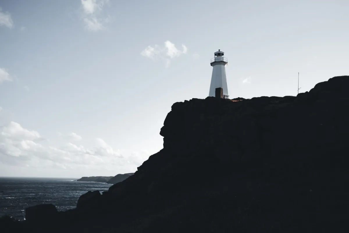 White lighthouse standing on a dark cliff above the ocean