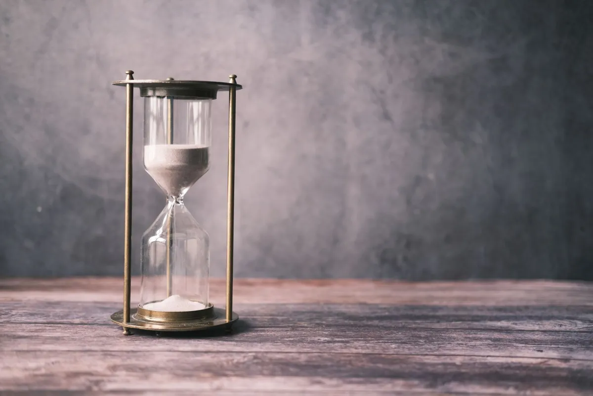 Hourglass on a wooden table against a gray wall