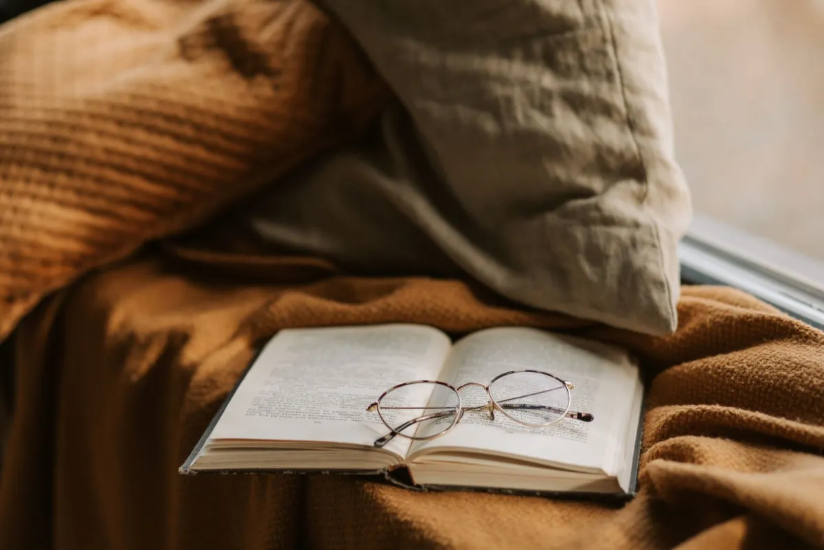 Окуляри для читання лежать на розкритій книжці на м'якому пледі