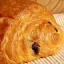 Primer plano de un croissant de chocolate dorado sobre una superficie de madera.